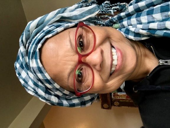 Woman with red glasses and a blue and white head scarf smiles